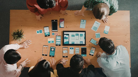 Diverse group of professionals gathered around a wooden table collaborating on a mobile app...