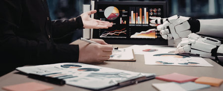 Human and robotic hand collaborate on data analysis project surrounded by charts and graphs on...