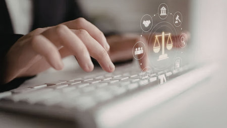 Person typing on a laptop keyboard with digital icons related to law and justice overlaid on the...
