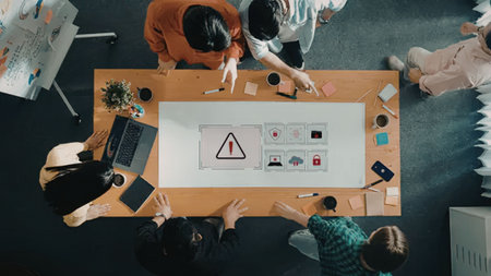 Group of young professionals gathered around a table discussing cybersecurity threats and solutions,...