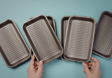 Multiple metal food trays held by hands on a bright blue background