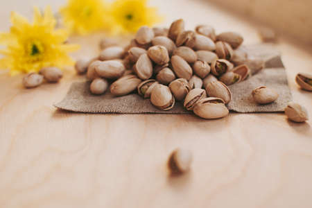 Small handful of pistachios on the wooden surface with yellow flowers.の写真素材