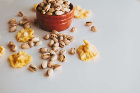Handful of pistachios in a brown vase, some pistachios on the table with pineapples.の写真素材
