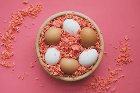 White and brown easter eggs in a wooden bowl on coral surface.
