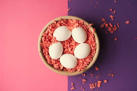 White easter eggs in a wooden bowl on pink and purple surface.