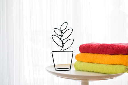 Bath towels of different colors close to a decorative flower on a light gray background.の写真素材
