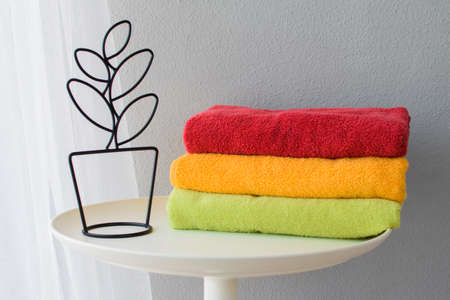 Bath towels of different colors close to a decorative flower on a light gray background.の写真素材