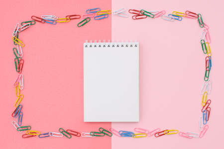 Blank notepad in a frame of colored paper clips on a double background - pink and coral. Concept...