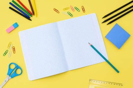 Notebook in a cage with a pencil, eraser, ruler, paper clips and other office supplies on a yellow...