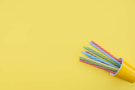 Yellow paper cup with some striped tubes lies on a yellow background. Place for text.