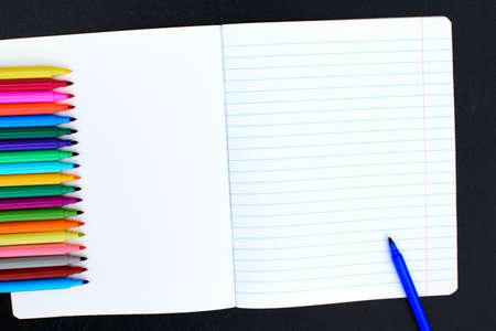 Open multicolored markers closeup on an open notebook in the line. Place for text.