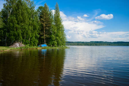 Blue simple boat on the shore of a lake somewhere in the depths of Finland, a good summer day. Vacation on the lake.の写真素材