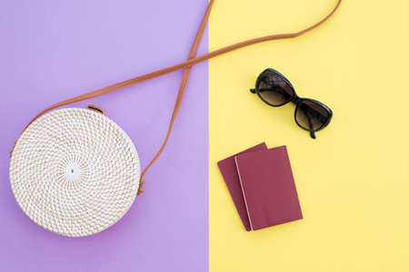 Beautiful round straw handbag and sunglasses with passports  on the yellow-purple background. Trendy handbag.の写真素材