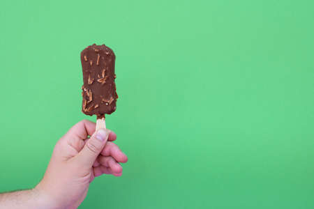 Hand of man holds chocolate ice cream on a stick, as eskimo, on a green surface background.の写真素材