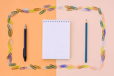 Notebook in cage with a pen and pencil in a frame of colored paper clips on a double background -...