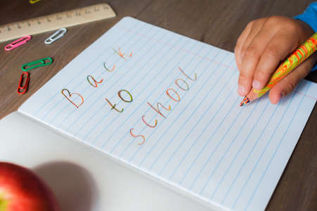 Open notebook, the page which is written Back to school, and the child hand with a colored pencil.