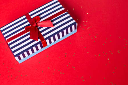 Gift striped box with a red satin bow and with lots of small stars on the red background.