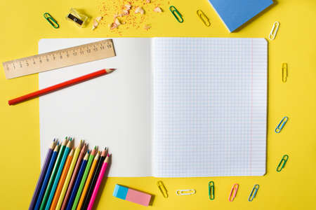 Notebook in a cage with a pencil, eraser, ruler, paper clips and other office supplies on a yellow...