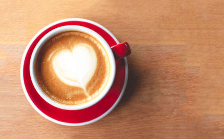A cup of cappuccino with latte art on a wooden background. Beautiful foam, red ceramic cup. Flat lay.の写真素材