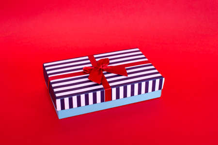 Gift striped box with a red satin bow on the red background.の写真素材