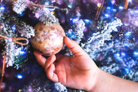 Children hand holding a Christmas toy ball, which hangs on a Christmas tree branch. Christmas...
