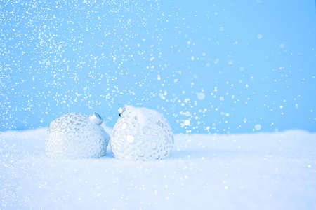 White Christmas balls with a beautiful pattern lies on the white snow with sparkles on the blue background. Christmas and New Year concept.の写真素材