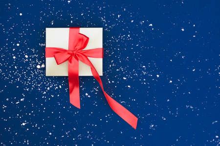 Gift gold box with a red satin bow on the snowy blue background.