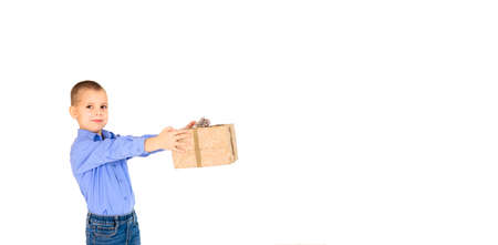 A boy in a purple shirt holding a gift from craft paper in his outstretched hands on a white background, isolated on white. Holiday concept. Banner.の写真素材