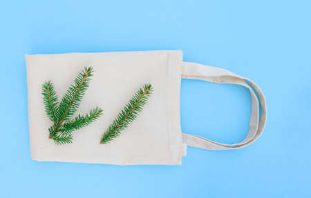 Canvas cotton white bag and branch of Christmas tree on bright blue background. Eco Friendly reusable bag for groceries. Eco and zero waste concept.の写真素材