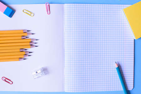 Notebook in a cage with a pencil, eraser, ruler, paper clips and other office supplies on a blue background. Concept back to school. Place for text.の写真素材