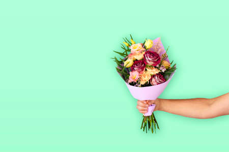 Hand of the man holding a beautiful bouquet of flowers on a green mint background. Flowers to gift. Place for text. の写真素材