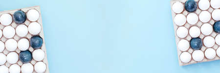 A lot of white eggs and a few painted in blue are in the container on the light blue background. Top...