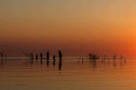 Silhouette of a big family walking on the lake at sunset. Concept of traveling family and enjoying the outdoors and the nature.の写真素材