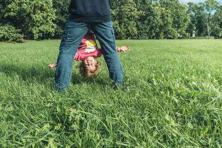 Father and daughter spending time on the field. Father holding daughter upside down. She is smiling. Concept of friendly family. Great family vacation.の写真素材