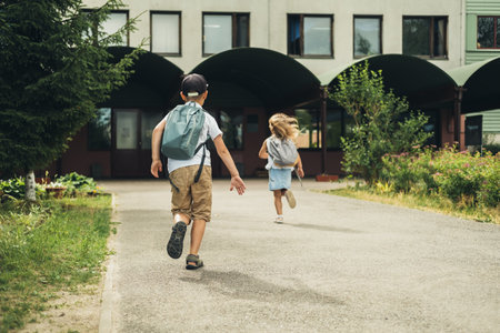 Two caucasian children, boy and girl, running to school with bags behind their backs. Students are ready for the new year. Back to school.の写真素材