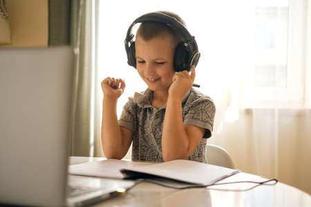 School boy in headphones using laptop while doing schoolwork at home or during online lesson. Online education concept.の写真素材