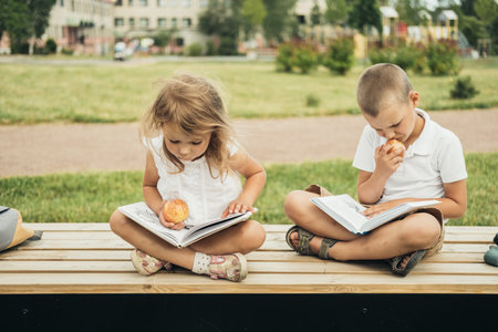 Two caucasian little students, boy and girl, eating apples during school break and reading books. Students are ready for the new year. Back to school.の写真素材