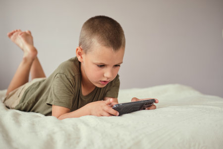 Young boy lying on the bed and playing or watching video in smartphone. Internet communication, modern technologies and people concept.の写真素材
