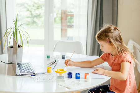 Young cute girl spending a time drawing using online lessons on laptop. Distance learning, online education.の写真素材