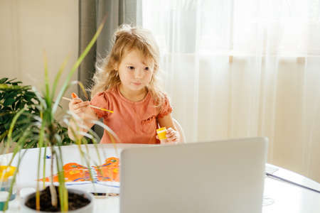 Young girl spending a time drawing using online lessons on laptop at home. Distance learning, online education.の写真素材