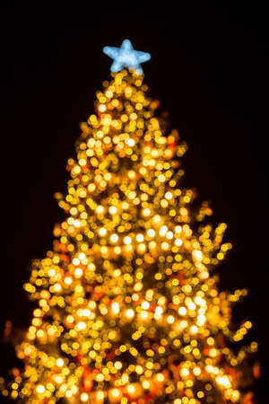 Defocused background of Christmas tree with garlands and star. Glowing illumination bokeh. Atmospheric christmas eve.の写真素材