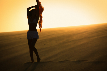 Woman silhouette with scarf in the hand in sunset on sand dune/ health nice woman bodyの写真素材