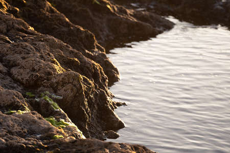 The calm sea water bathes a group of rocks with moss at sunset. Concept of peace, tranquility.の写真素材