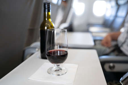 A glass with red wine and a small bottle in the background on the table of a passenger in an airplaneの写真素材