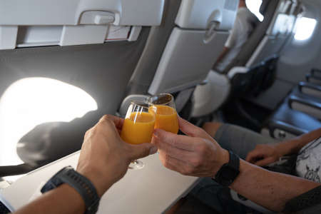 Two hands toast with glasses of orange juice on a plane trip.の写真素材