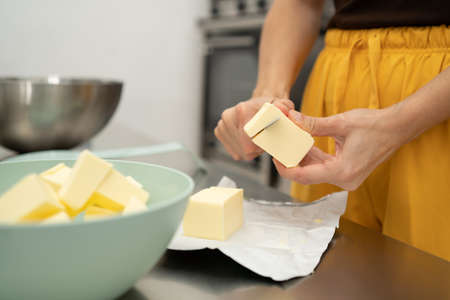 hands cutting butter with a red knife in a kitchen with unfocused background utensils. Concept of cooking, pastry.の写真素材