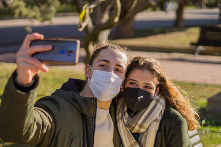 Young couple taking a selfie in the park with antivirus surgical mask