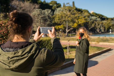 Man taking pictures of a woman in the park with his smartphone with surgical maskの写真素材