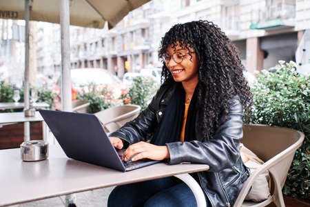 black girl with curly hair working in a bar with her laptopの写真素材