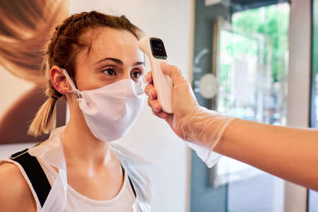 Woman checking temperature to a client using infrared tool in beauty salon - social distancing conceptの写真素材
